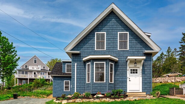A two-story house with a gabled roof, a front porch, and a small garden area with rocks and plants.
