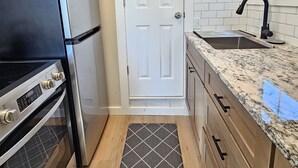 A compact kitchen with white cabinets, a black refrigerator, a stainless steel oven, a granite countertop, a black faucet, and a patterned rug.