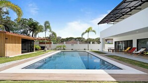 A modern outdoor swimming pool with a clear blue water surface, surrounded by well-maintained grass and a wooden deck. - Casa Corales Dreams Deluxe (Playa Flamingo)