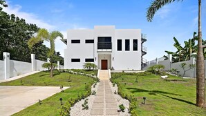 A modern building with a central entrance, surrounded by a well-maintained garden with a stone pathway leading to the door. - Casa Corales Dreams Deluxe (Playa Flamingo)