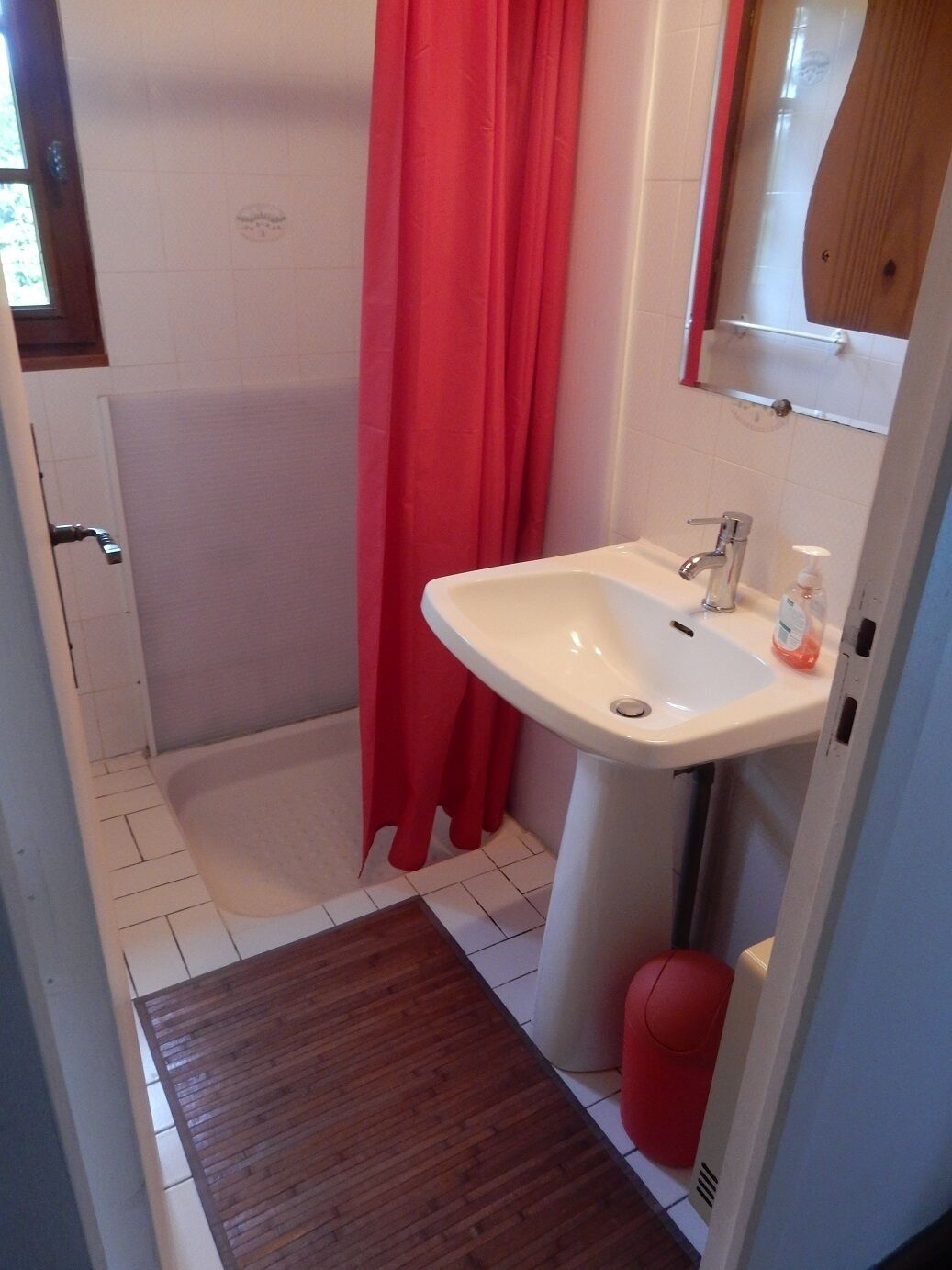 A bathroom with a white sink, a red shower curtain, and a wooden floor.
