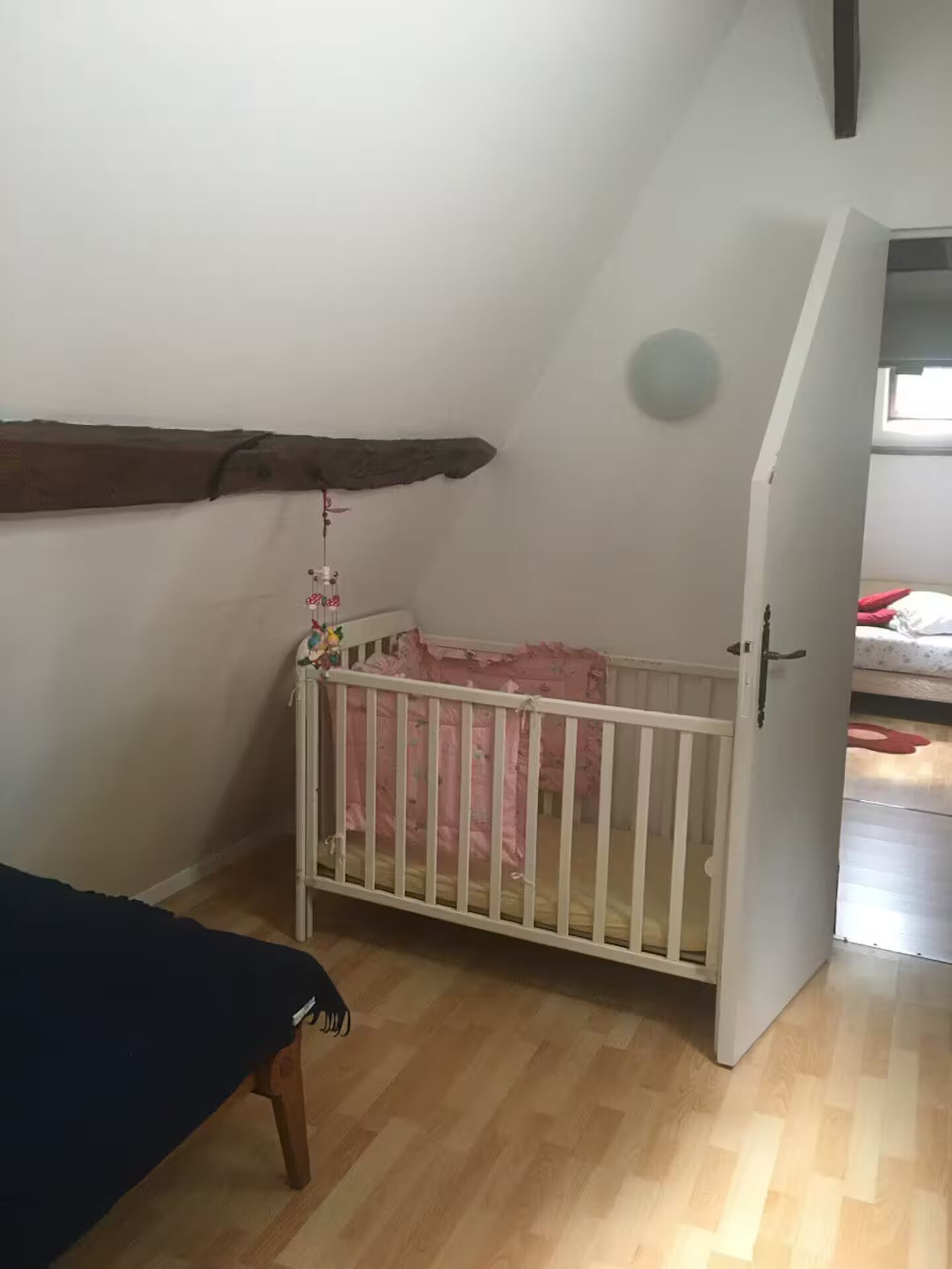 Habitación con una cuna, piso de madera y una puerta que da a otra habitación.