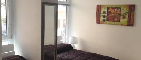 A room with two beds, a large mirror, a painting on the wall, and a window.