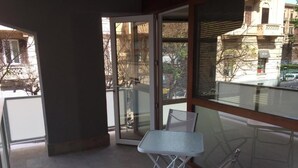 Un balcón con una mesa, sillas, un ventanal de vidrio y vistas a edificios y árboles.