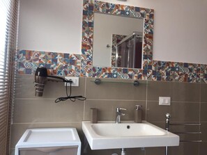 Een badkamer met een wit wastafel, een spiegel en een haardroger op een wandhouder.