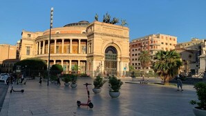Una plaza pública con un edificio histórico que presenta columnas y una gran entrada arqueada.