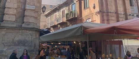 Un marché de rue avec des étals et un bâtiment historique portant une inscription indiquant « Porta Carini ».