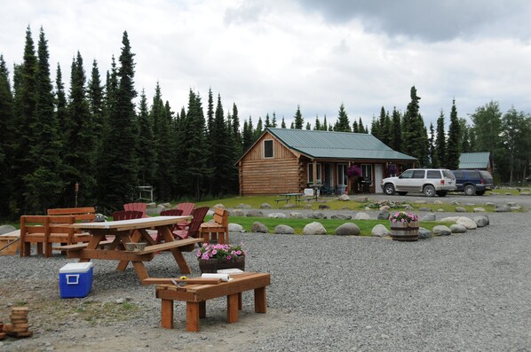 A rustic cabin with a gravel patio, picnic tables, and outdoor seating. - Alaska Red Fish Lodge Furnished 2 Bedroom Cabin #2 (Sterling)