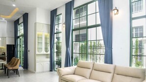 Un salon spacieux avec un canapé beige, un coin repas comprenant une table et des chaises, et de grandes fenêtres ornées de rideaux bleus.