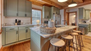 Une cuisine spacieuse dotée d’un grand îlot central, de meubles de couleur verte et de poutres en bois au plafond.