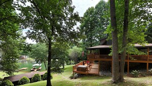 Une cabane dotée d’une terrasse donnant sur un étang, entourée d’arbres.