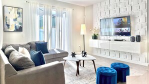 Ein modernes Wohnzimmer mit Sofa, Couchtisch, Poufs, Fernseher und Deckenventilator.