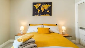 Une chambre d’hôtel avec un lit, deux tables de chevet avec des lampes, une carte du monde accrochée au mur et une pile de serviettes sur le lit.