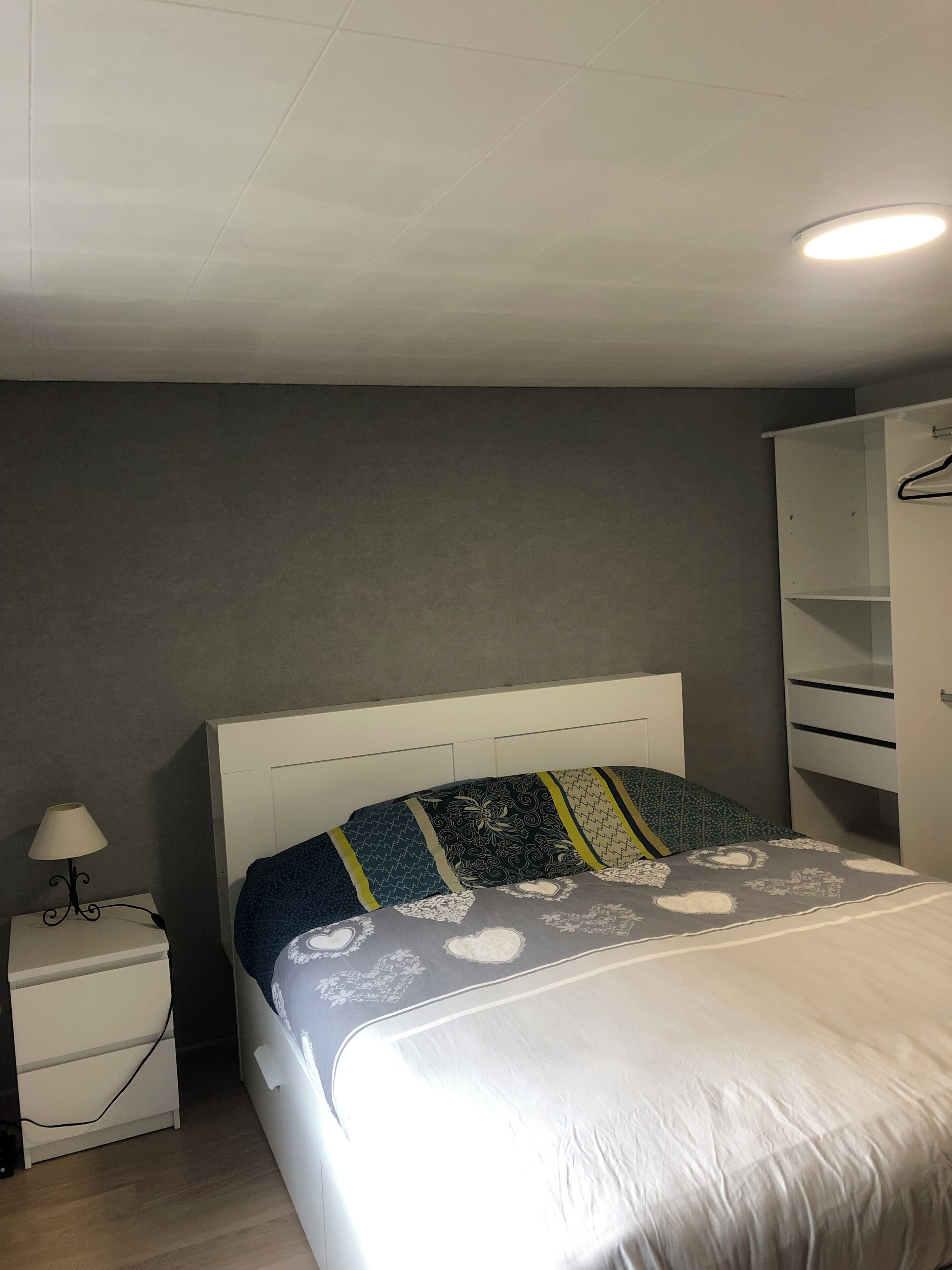 A bedroom with a bed, bedside table, lamp, and wardrobe.