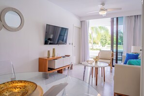 A modern living room with a flat-screen TV, a round mirror, a glass coffee table, and a sofa with blue cushions. - Charming 2-bedroom Apartment w/ Private Jacuzzi AC, Wi-Fi in Gorgeous Punta Cana (Punta Cana)