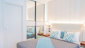 A modern hotel room with a large bed, a mirror, bedside tables, and a nightstand.