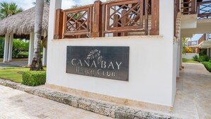A sign for Canabay Beach Club with a palm tree and a thatched roof structure in the background.