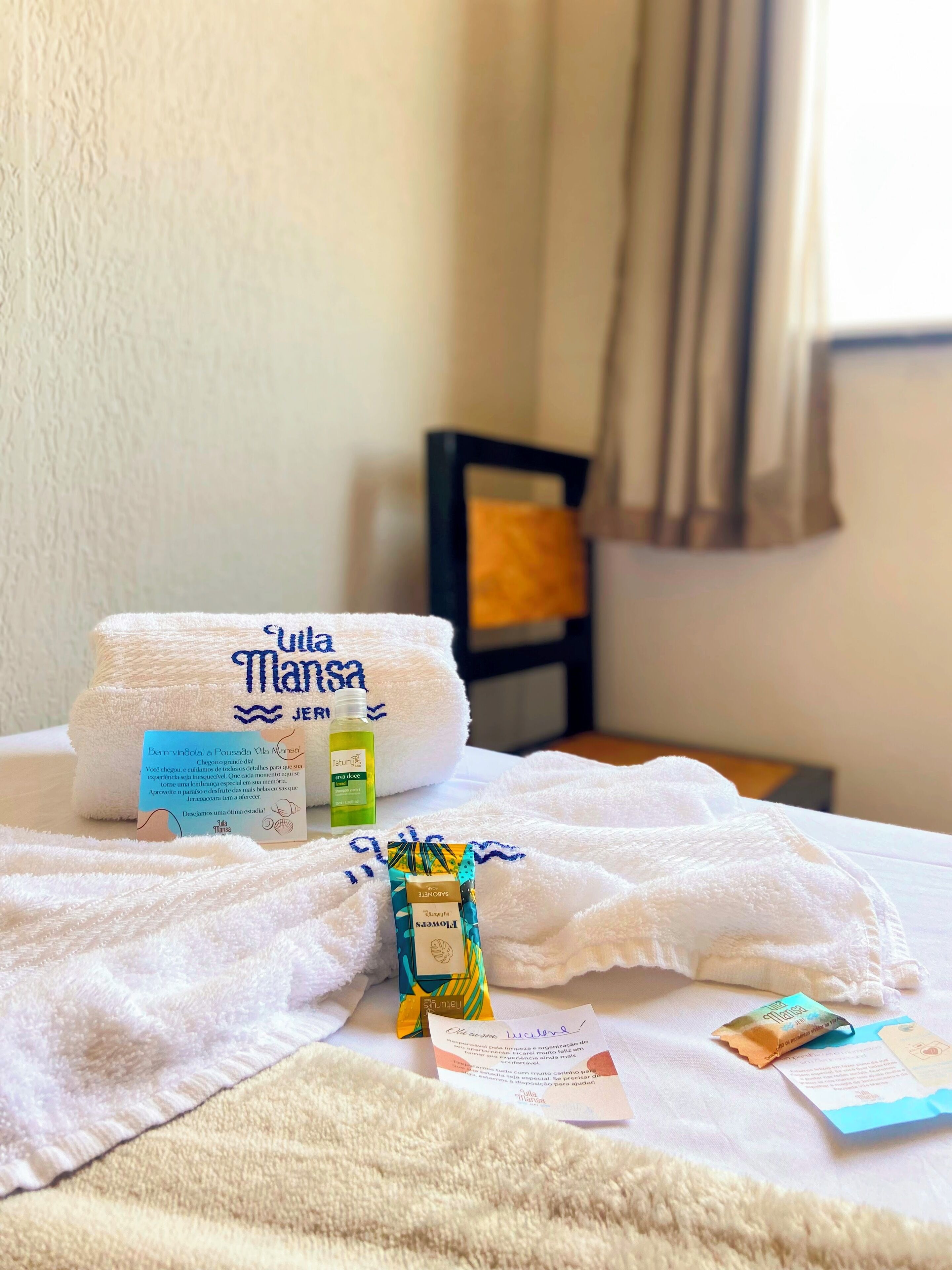 A neatly made bed with a white towel, a bottle of lotion, and a packet of shampoo.