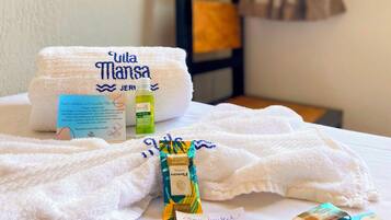 A neatly made bed with a white towel, a bottle of lotion, and a packet of shampoo.