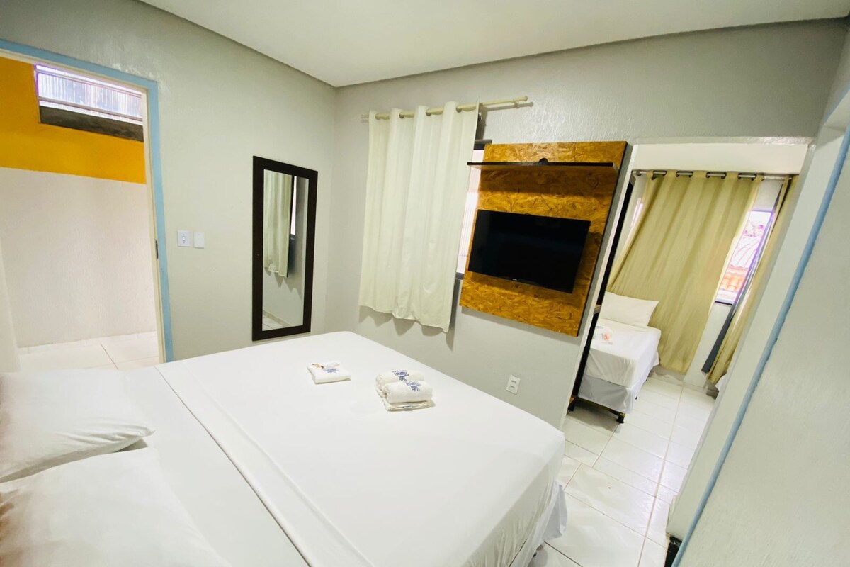 A hotel room with a bed, a TV mounted on a wooden panel, a mirror, and a window with curtains.