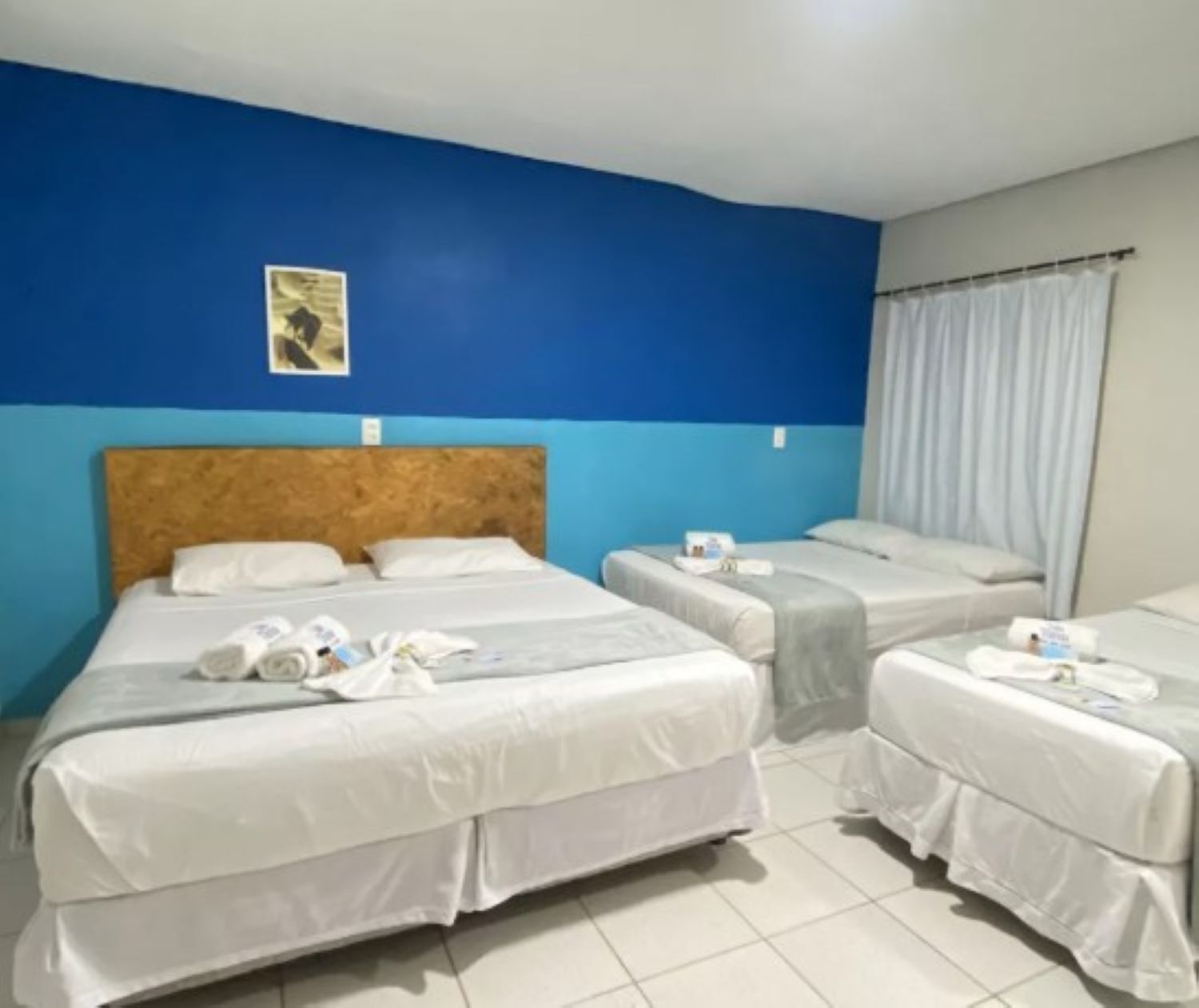 Habitación de hotel con tres camas, una pared azul decorativa y una cortina en la ventana.