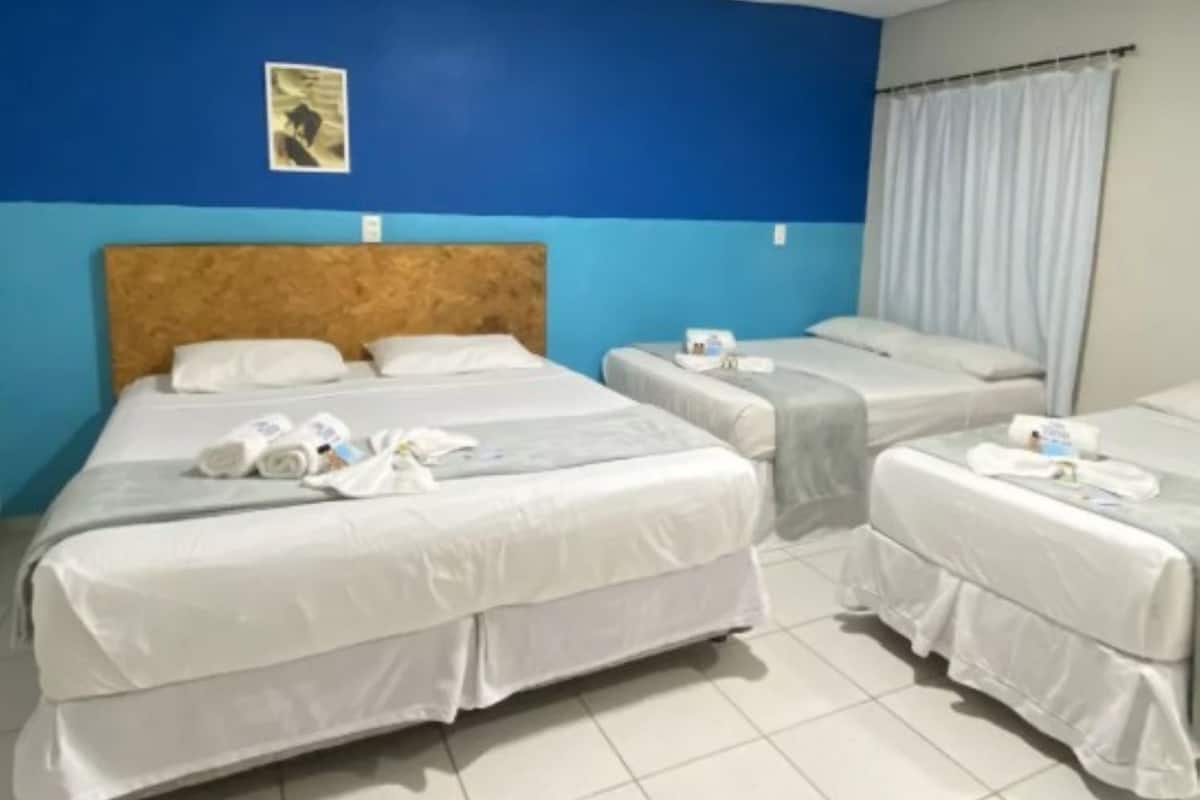 Une chambre d’hôtel avec trois lits, un mur d’accent bleu et un rideau à la fenêtre.