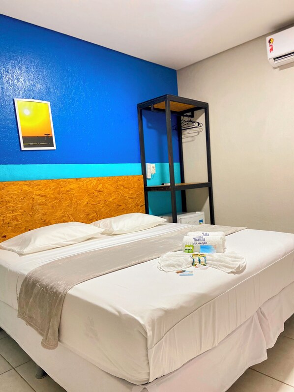 A hotel room with a bed, a wooden headboard, a blue wall, a white air conditioner, and a framed picture on the wall. - Pousada Vila Mansa Jeri (Jijoca de Jericoacoara)