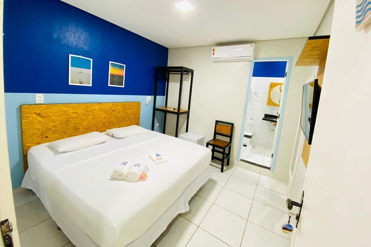 Une chambre d’hôtel équipée d’un lit, d’une chaise, d’une étagère et d’un appareil de climatisation.