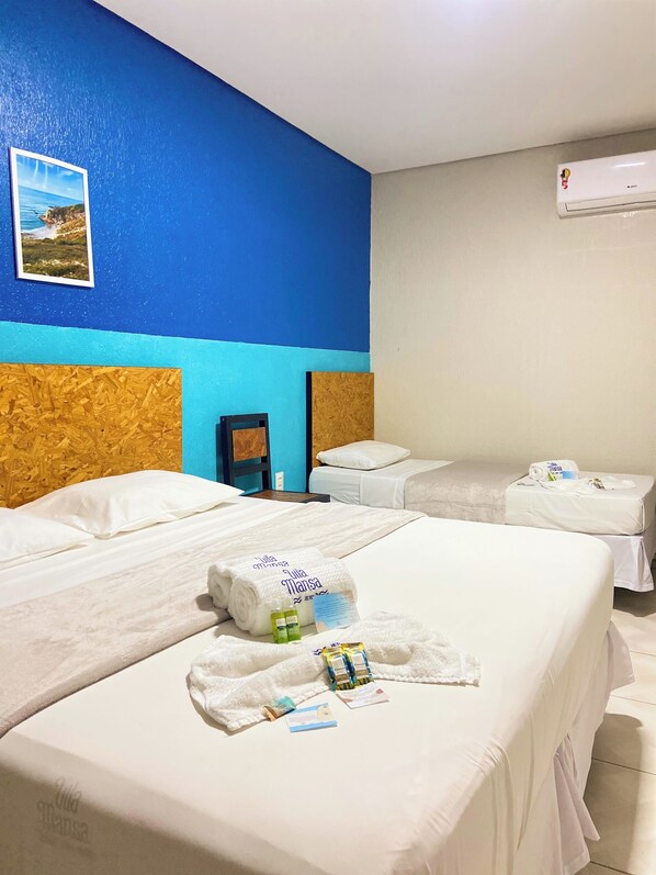 A hotel room with two beds, a blue and white color scheme, an air conditioning unit, and a framed picture on the wall.