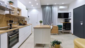 Une cuisine moderne dotée d’un îlot central, d’un four encastré et d’appareils électroménagers en acier inoxydable. On y trouve également un coin repas avec une chaise verte et une petite table.