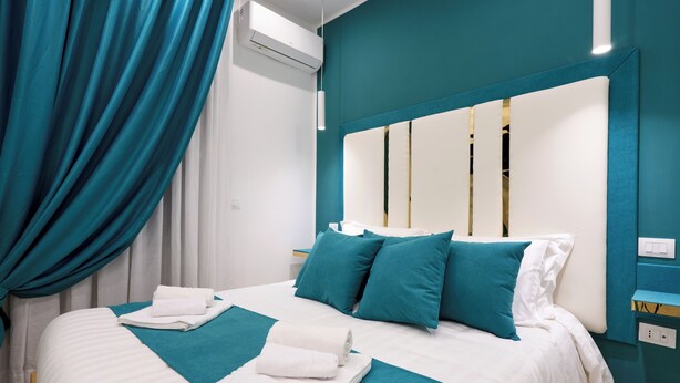 Une chambre d’hôtel avec un lit, des rideaux de couleur turquoise, du linge de lit blanc et un grand miroir au-dessus du lit.