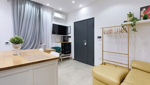 Une chambre d’hôtel moderne avec un bureau en bois, un canapé, une télévision, une armoire et une plante.