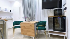 Une cuisine moderne avec une table en bois, deux chaises vertes, un four à micro-ondes et un téléviseur fixé au mur.