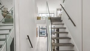 Ein modernes Interieur mit einer Treppe, die zu einer zweiten Etage führt, inklusive Glastrennwand und Holzbodenstufen.