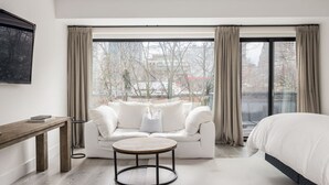 Ein modernes Hotelzimmer mit einem großen Fenster, einem weißen Sofa, einem runden Couchtisch und einem Bett.