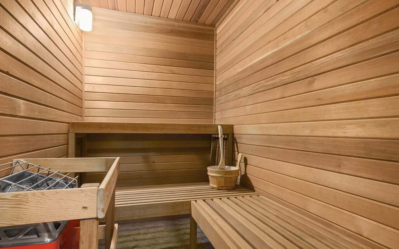 A sauna with wooden walls, a bench, a bucket, and a metal rack.