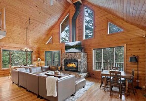 A log cabin interior with a stone fireplace, a large sofa, and a dining table. - Summit Log Cabin With Hot Tub & Sauna (Snoqualmie Pass)