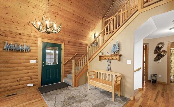 A wooden interior with a staircase, a bench, a chandelier, and a door. - Summit Log Cabin With Hot Tub & Sauna (Snoqualmie Pass)