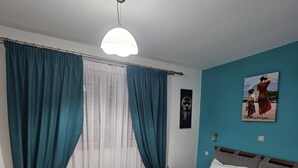 A bedroom with a bed, curtains, a painting, and a ceiling light.