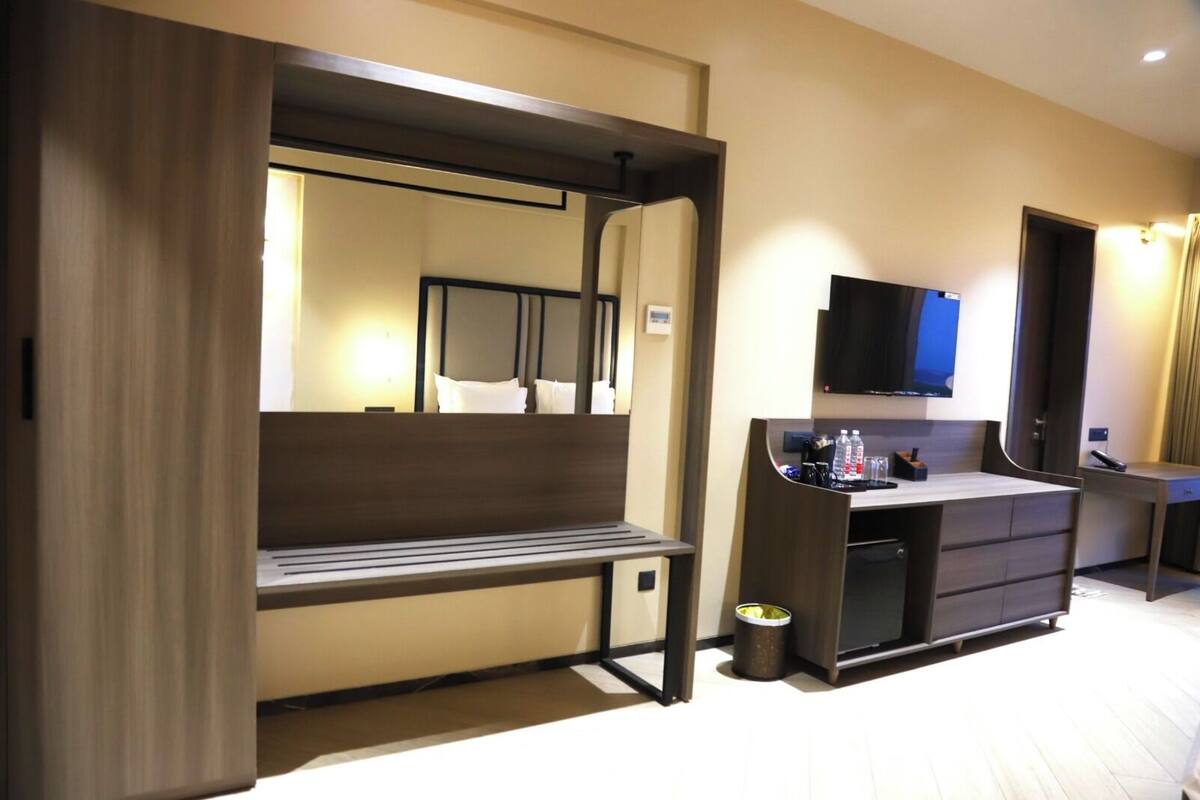 Une chambre d’hôtel avec un banc en bois, un bureau doté d’un téléviseur à écran plat, une poubelle et un mini-bar.