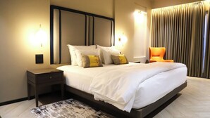 Moderni hotellihuone, jossa on suuri sänky, yöpöydällä olevat lamput, yöpöytä ja näkymä kaupunkiin verhojen läpi.