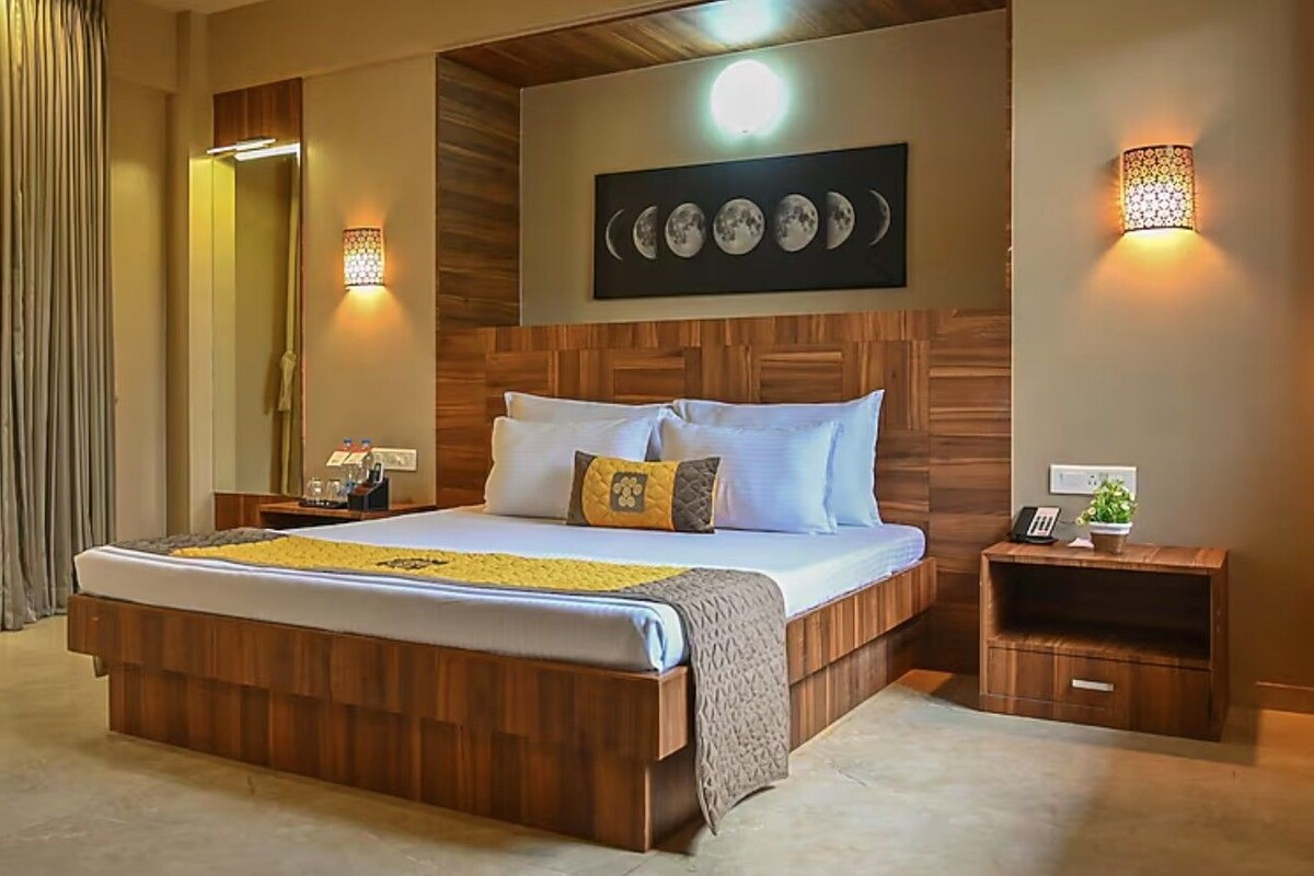 A hotel room with a wooden bed, a nightstand with a phone and a lamp, and a wall-mounted artwork depicting the moon phases.