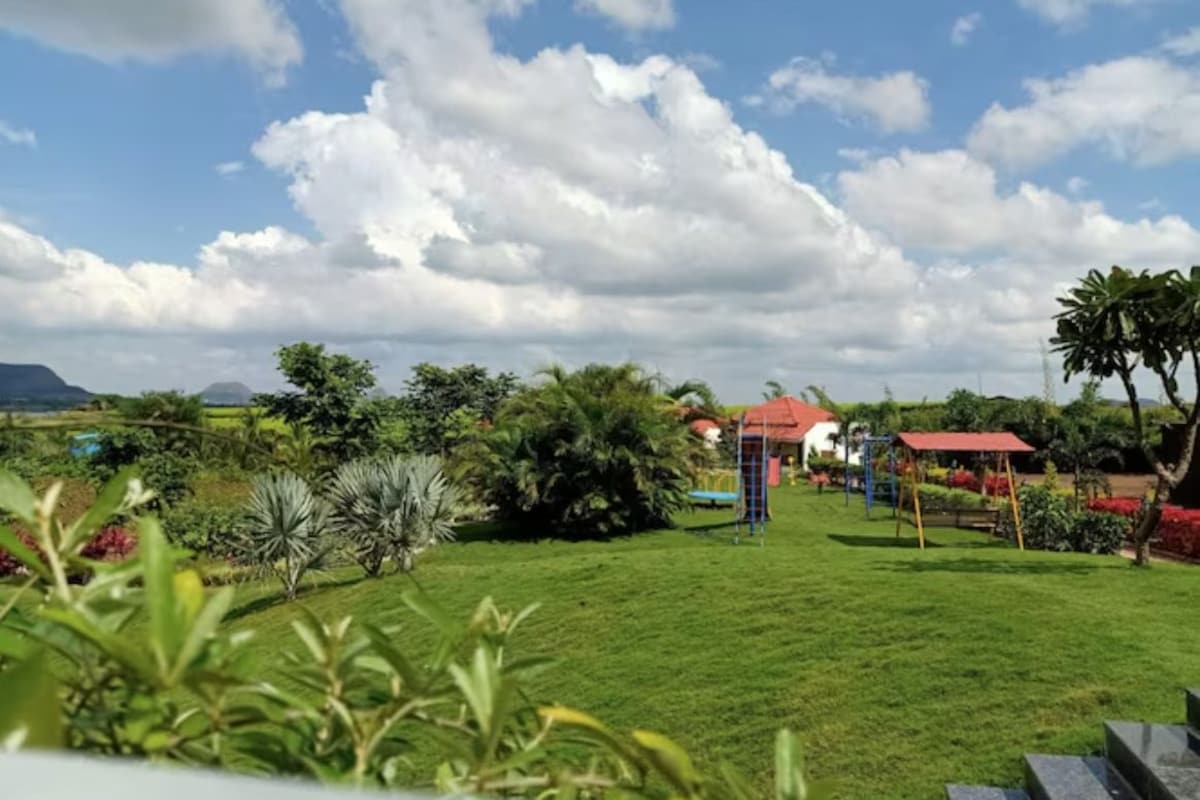 A grassy outdoor area with a playground, a red-roofed building, and a clear sky.
