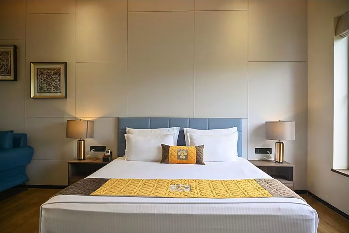 A hotel room with a large bed, two bedside tables with lamps, a blue headboard, and a blue armchair.