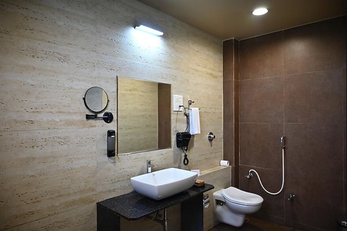 A modern bathroom with a large mirror, a white sink, a toilet, and a shower.