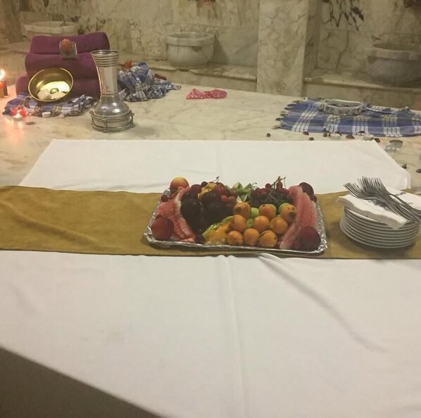 A table set with a variety of fruits and a silver tray, surrounded by a white tablecloth and a brown cloth. - Aydıner Resort Otel (Horasan)