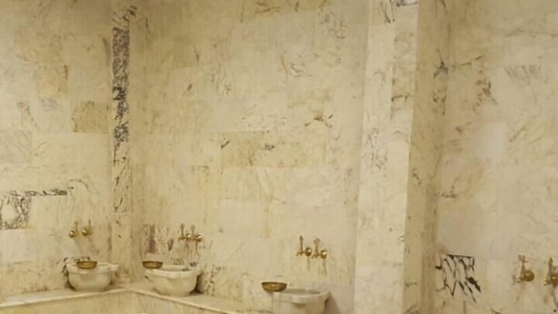 Een marmeren badkamer met een groot centraal badkamermeubel, twee kleinere wastafels en een bad.