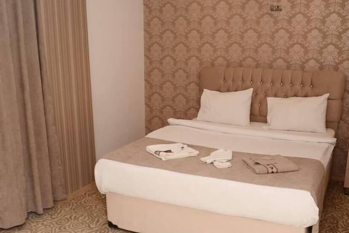 A neatly made bed with a headboard, a patterned carpet, and a curtain.