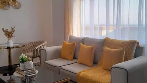A modern living room with a grey sofa, yellow cushions, a black coffee table, and a chandelier. - Lux Suites Zerubabel penthouse Kisumu (Kisumu)