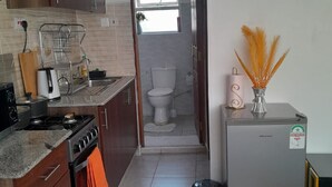 A compact kitchen with a stove, oven, and sink, leading to a small bathroom with a toilet and window. - Lux Suites Zerubabel penthouse Kisumu (Kisumu)